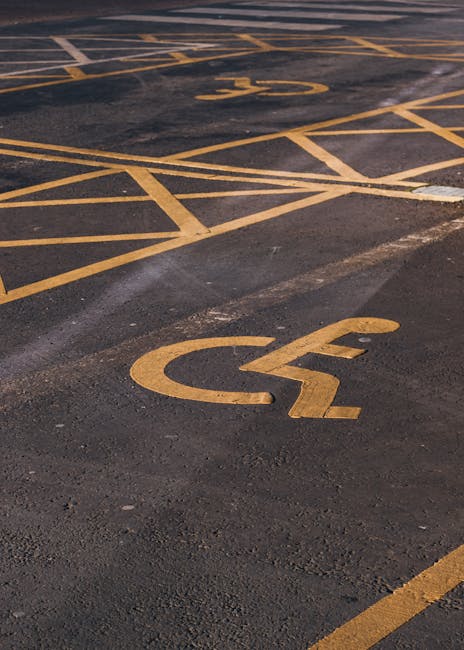 Close-up view of a yellow-painted disabled accessible parking symbol on an asphalt surface, with visible cracks and texture. The symbol's lines are slightly worn, indicating regular use. The image captures the parking area adjacent to a property, likely part of the access point for a home or commercial building involved in a nearby house removal or relocation process. No vehicles or other objects are visible in the frame. This type of marking is common in urban settings to designate spaces for relocating furniture or belongings during home relocation services provided by Man with Van Herne Hill. The lighting appears natural, suggesting daytime conditions, and the surface is clean without debris. The focus is on the parking designation, supporting the context of moving logistics and accessible parking during a professional removal service at Croxted Road.