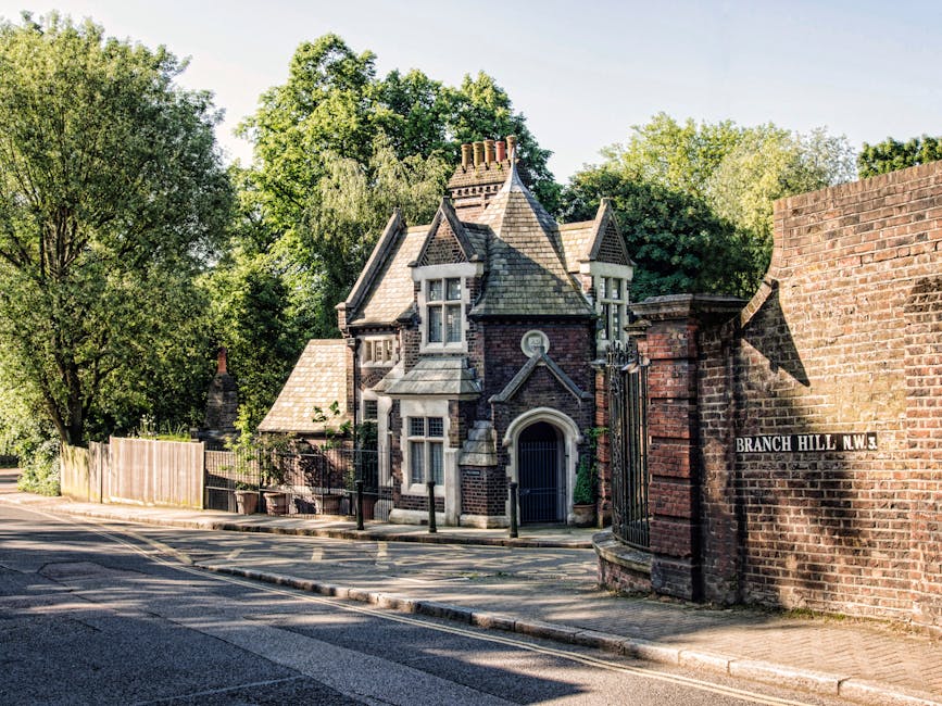 An exterior view of a Victorian-style residential property situated on a tree-lined street, with the house constructed from dark brick and featuring ornate architectural details, steeply pitched roofs