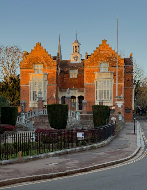 An exterior view of a Victorian-style residential property situated on a tree-lined street, with the house constructed from dark brick and featuring ornate architectural details, steeply pitched roofs